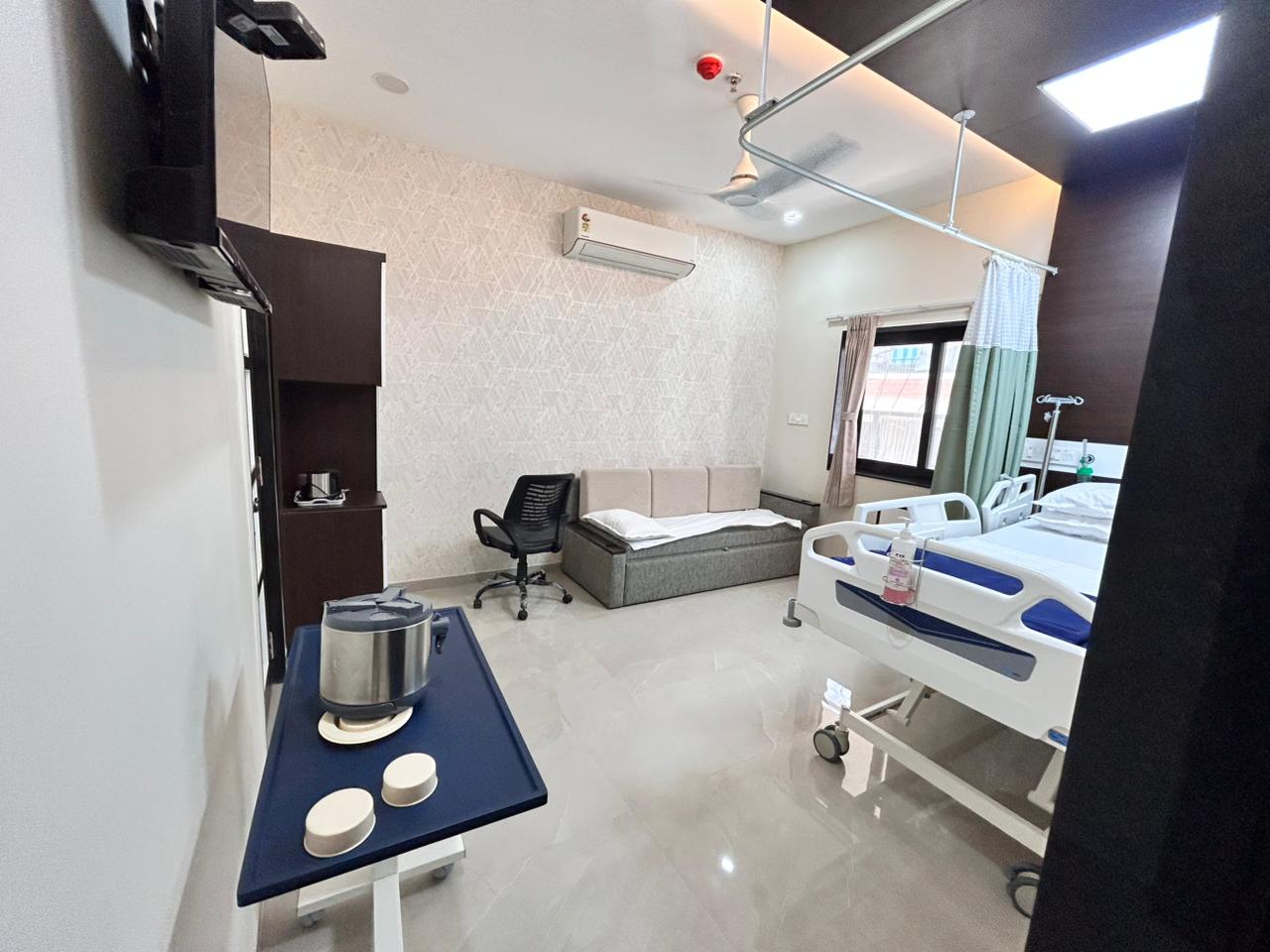 Patient room with wall-mounted TV, attendant sofa and sun-room view.